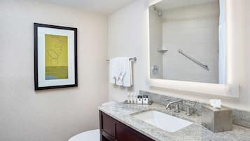 A modern bathroom with a marble sink, a large mirror, a framed artwork, and a white toilet.
