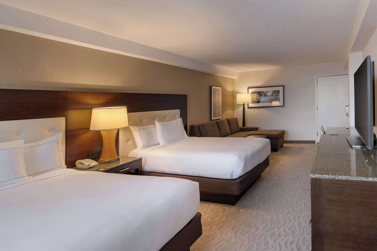 A hotel room with two beds, a desk, a television, and a lamp.