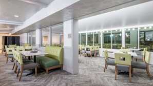 A modern dining area with green upholstered booths and wooden tables, large windows, and a herringbone-patterned floor. - Wyndham Garden Cross Lanes Charleston (Cross Lanes)