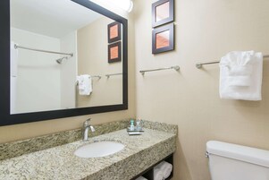 A bathroom with a granite countertop sink, a large mirror, a towel rack, and a toilet.