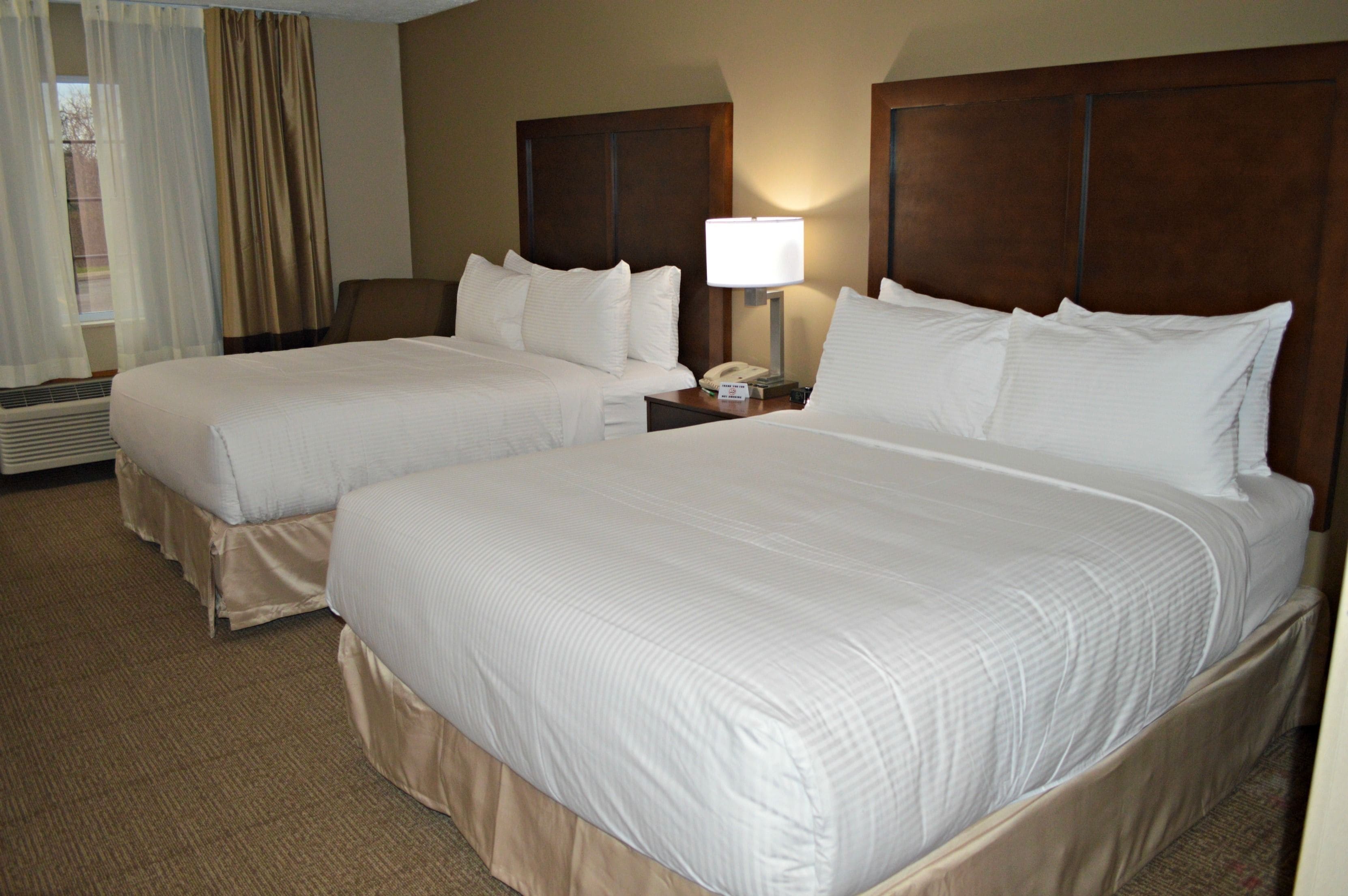 A hotel room with two beds, a nightstand with a lamp, and a window with curtains.