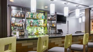 A bar area with multiple liquor bottles, a television, and bar stools. - Wyndham Garden Cross Lanes Charleston (Cross Lanes)