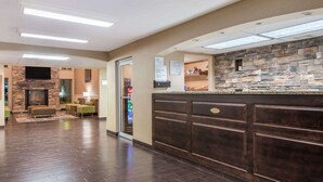 A lobby with a stone wall, a reception desk, and a seating area with green chairs. - Wyndham Garden Cross Lanes Charleston (Cross Lanes)