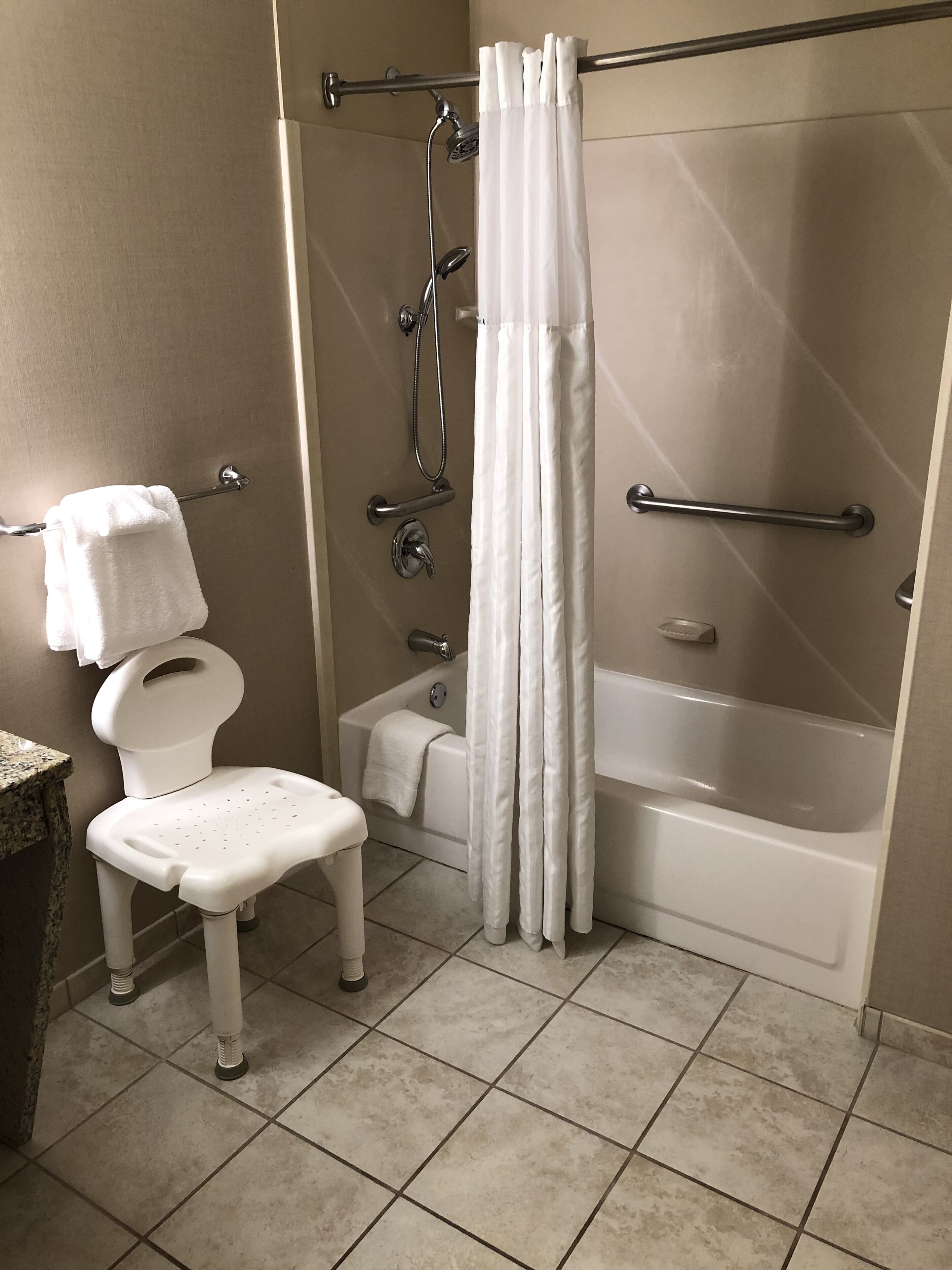 Ein Badezimmer mit Toilette, Duschstuhl, Badewanne und einer Duschkabine mit Vorhang.