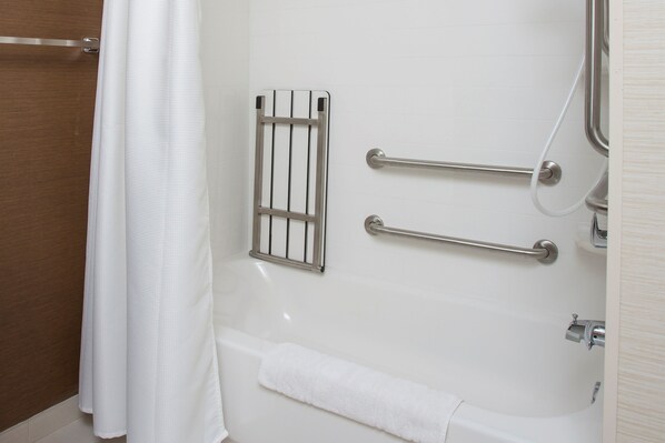Un baño con bañera, barras de apoyo, toallero y cortina de ducha.