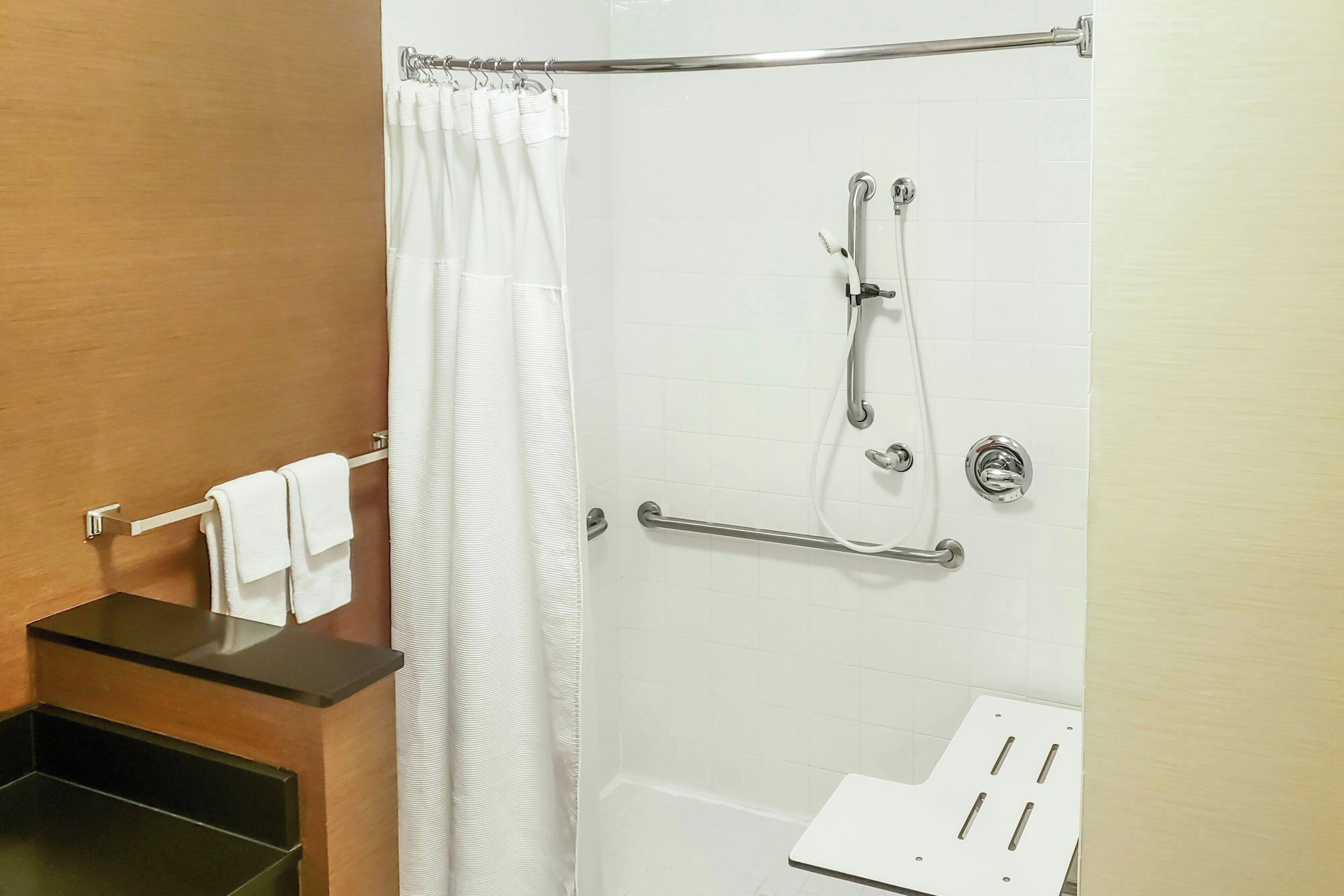Une douche équipée d’une barre d’appui, d’un porte-serviettes et d’un rideau de douche blanc.