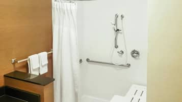 Une douche équipée d’une barre d’appui, d’un porte-serviettes et d’un rideau de douche blanc.