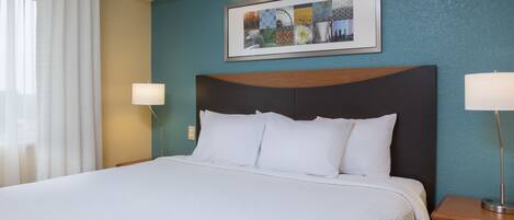 Uma cama bem arrumada com roupa de cama branca, uma cabeceira escura e duas luminárias de apoio.