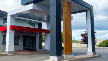Un edificio moderno con una columna vertical de madera destacada, un acento rojo en la fachada y un cielo despejado al fondo.
