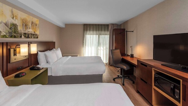 A hotel room with two beds, a desk with a flat-screen TV, a chair, and a painting on the wall.