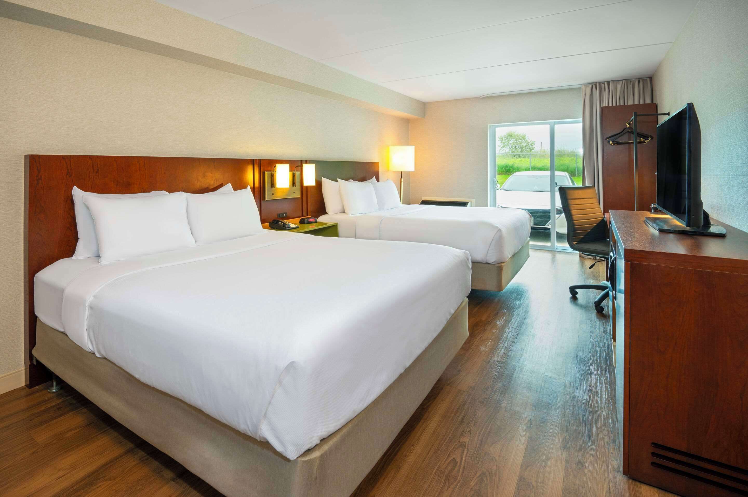 A hotel room with two beds, a desk with a TV, and a view of the outdoors.