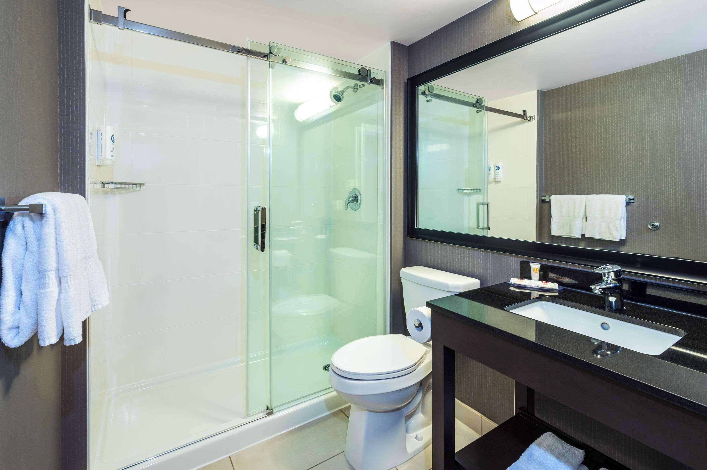 Un baño moderno con ducha de vidrio, inodoro blanco y lavamanos negro con espejo superior.