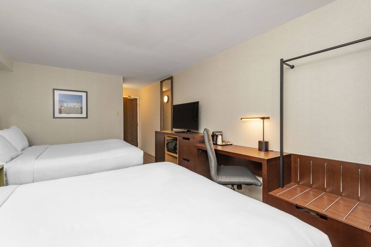 A hotel room with two beds, a desk with a chair, a television, and a lamp.