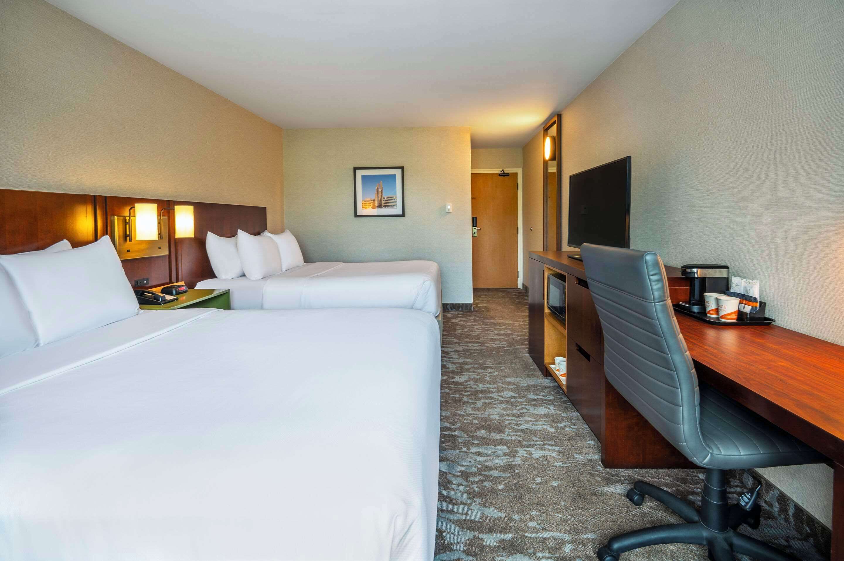 A hotel room with two beds, a desk with a chair, a TV, and a framed picture on the wall.