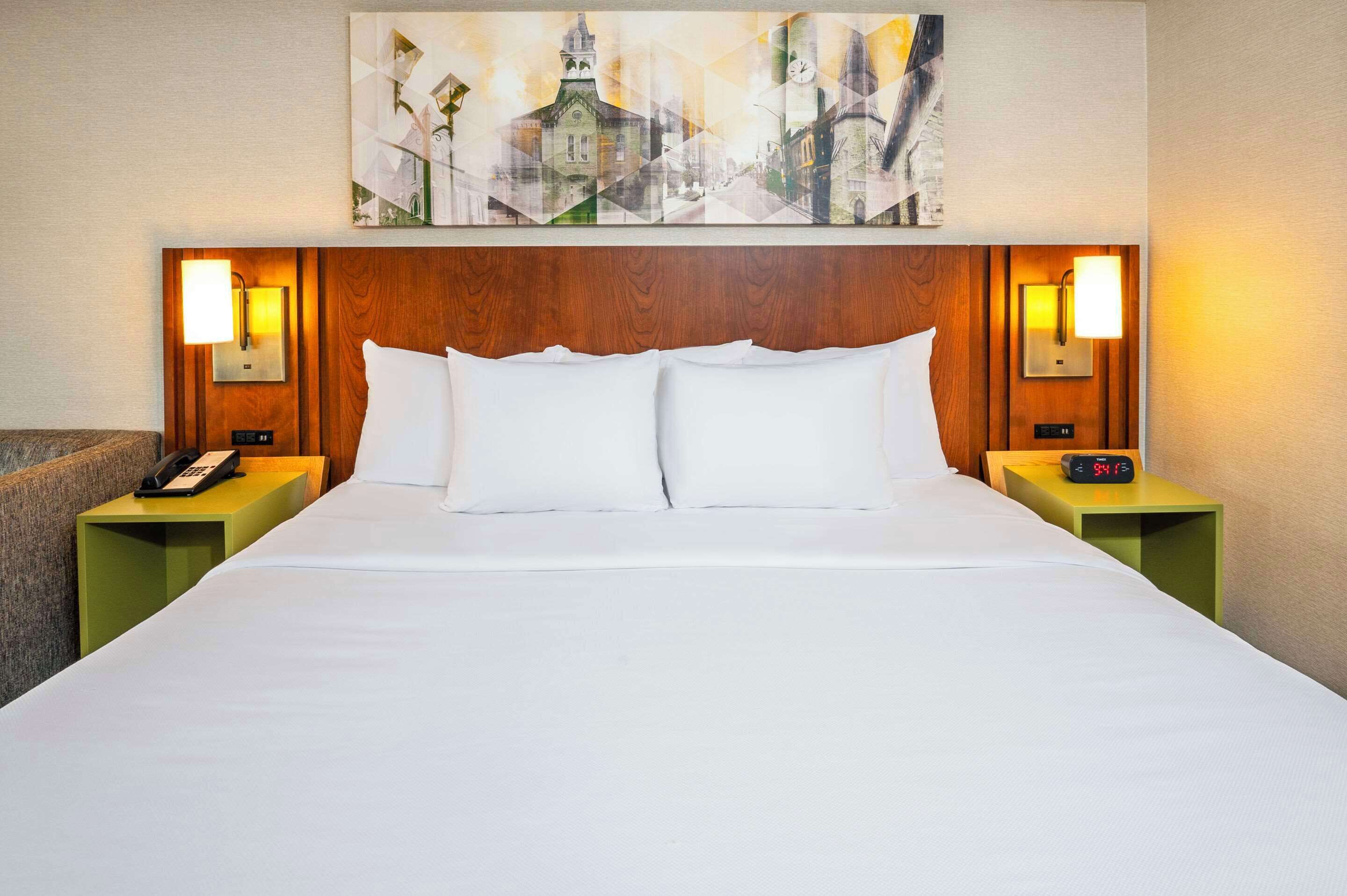 A hotel room with a large bed, two bedside tables with lamps, a telephone, and a painting above the bed.
