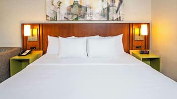A hotel room with a large bed, two bedside tables with lamps, a telephone, and a painting above the bed.