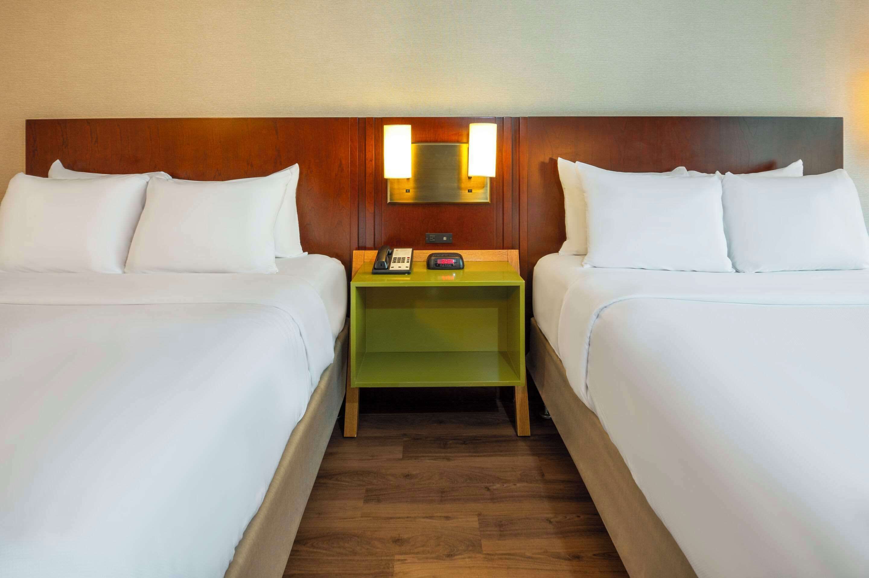 A hotel room with two beds, a green nightstand with a phone and a clock, and a wooden headboard.