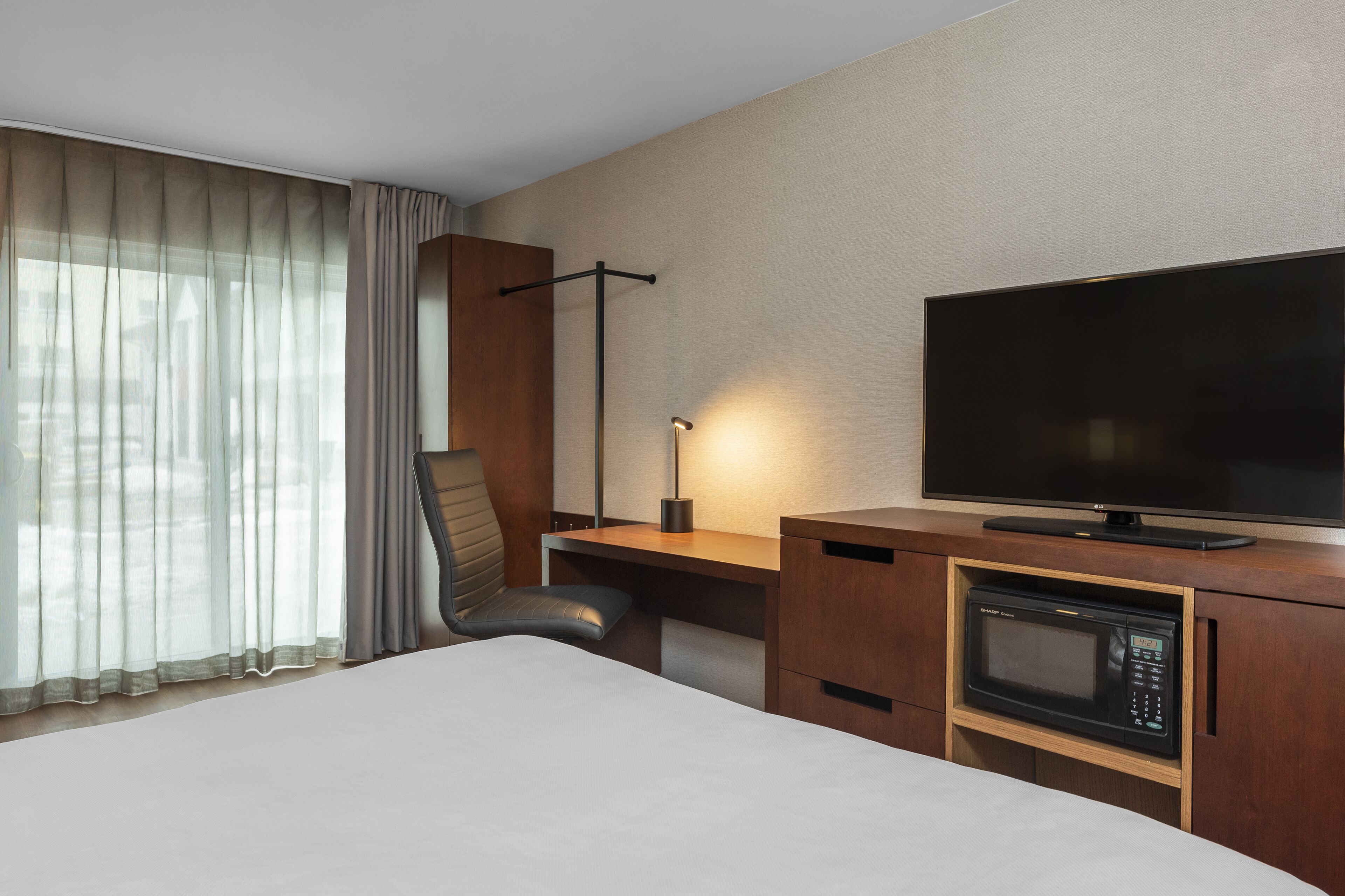 Habitació d'hotel amb llit, escriptori, televisió de pantalla plana, microones i una cadira.