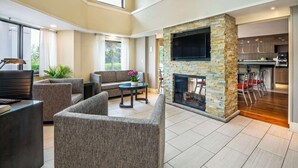 A spacious living area with a stone fireplace, comfortable seating, and a kitchen in the background.