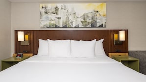 A hotel room with a large bed, two nightstands, a wall clock, and a painting above the bed.