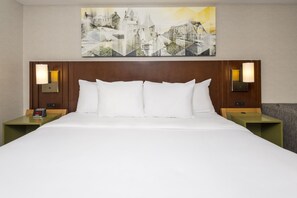 A hotel room with a large bed, two nightstands, a wall clock, and a painting above the bed.