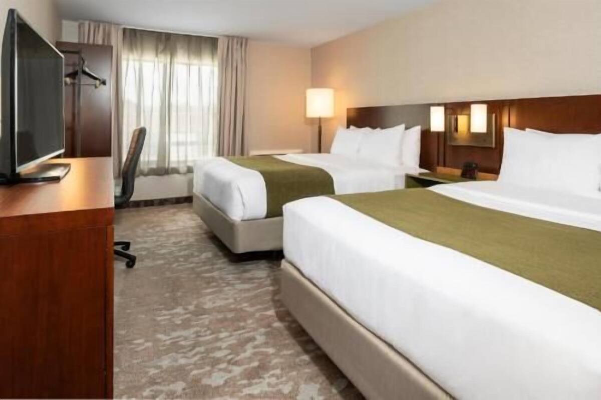 A hotel room with two beds, a desk with a television, a chair, and a lamp.