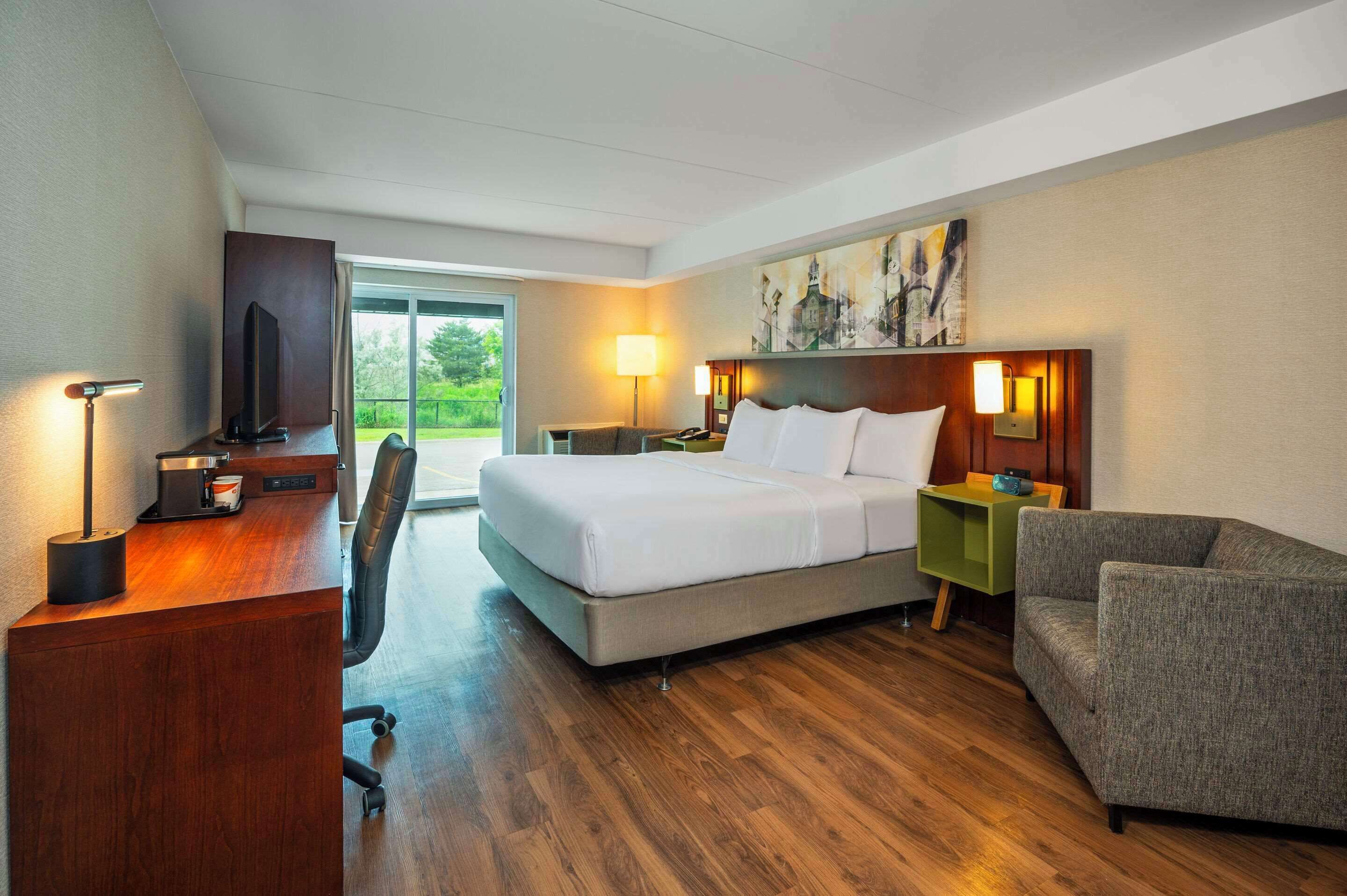A hotel room with a bed, desk, chair, and a painting on the wall.