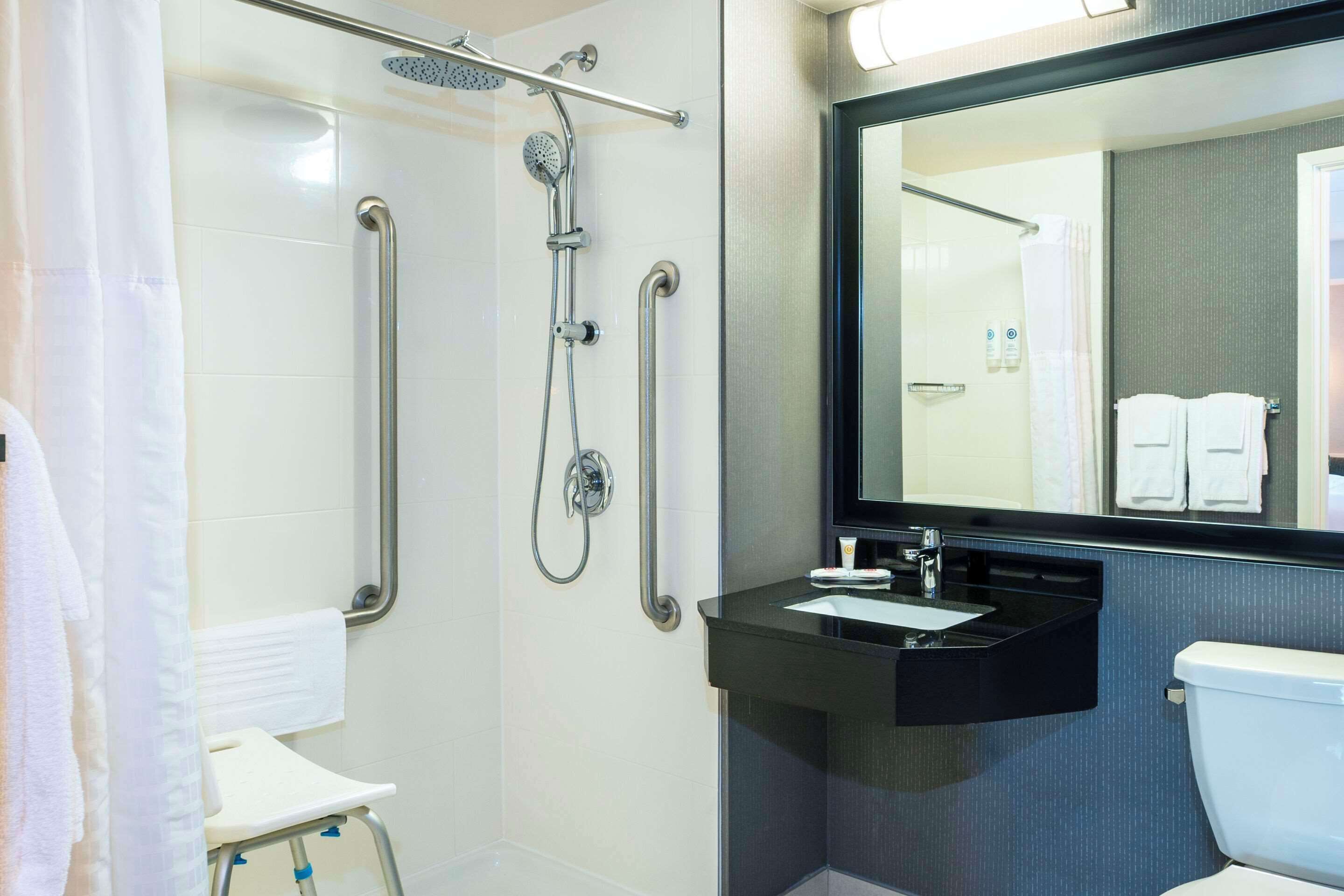 Un baño moderno con ducha a nivel, barras de apoyo, lavamanos e inodoro.