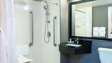 Un baño moderno con ducha a nivel, barras de apoyo, lavamanos e inodoro.