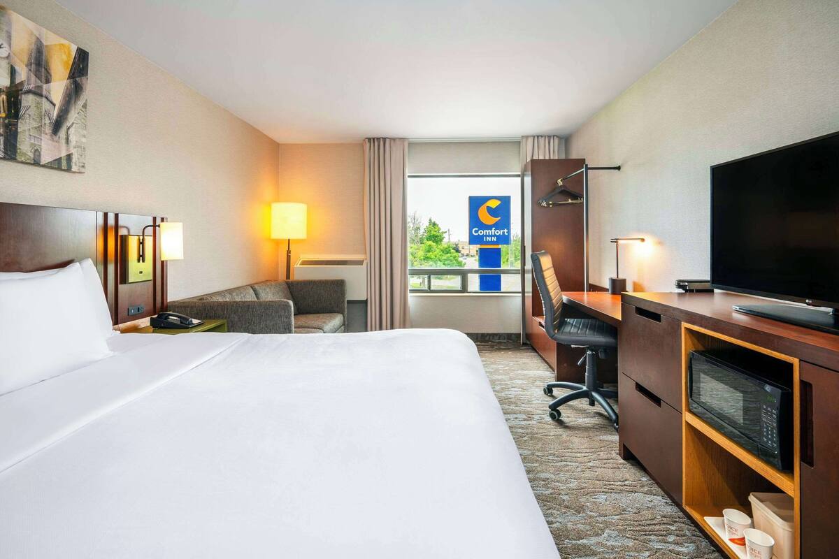 A hotel room with a bed, a desk with a computer, a TV, and a view of the city.