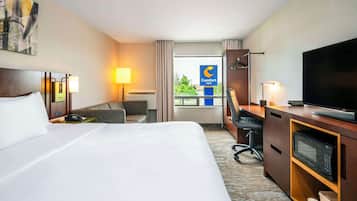 A hotel room with a bed, a desk with a computer, a TV, and a view of the city.