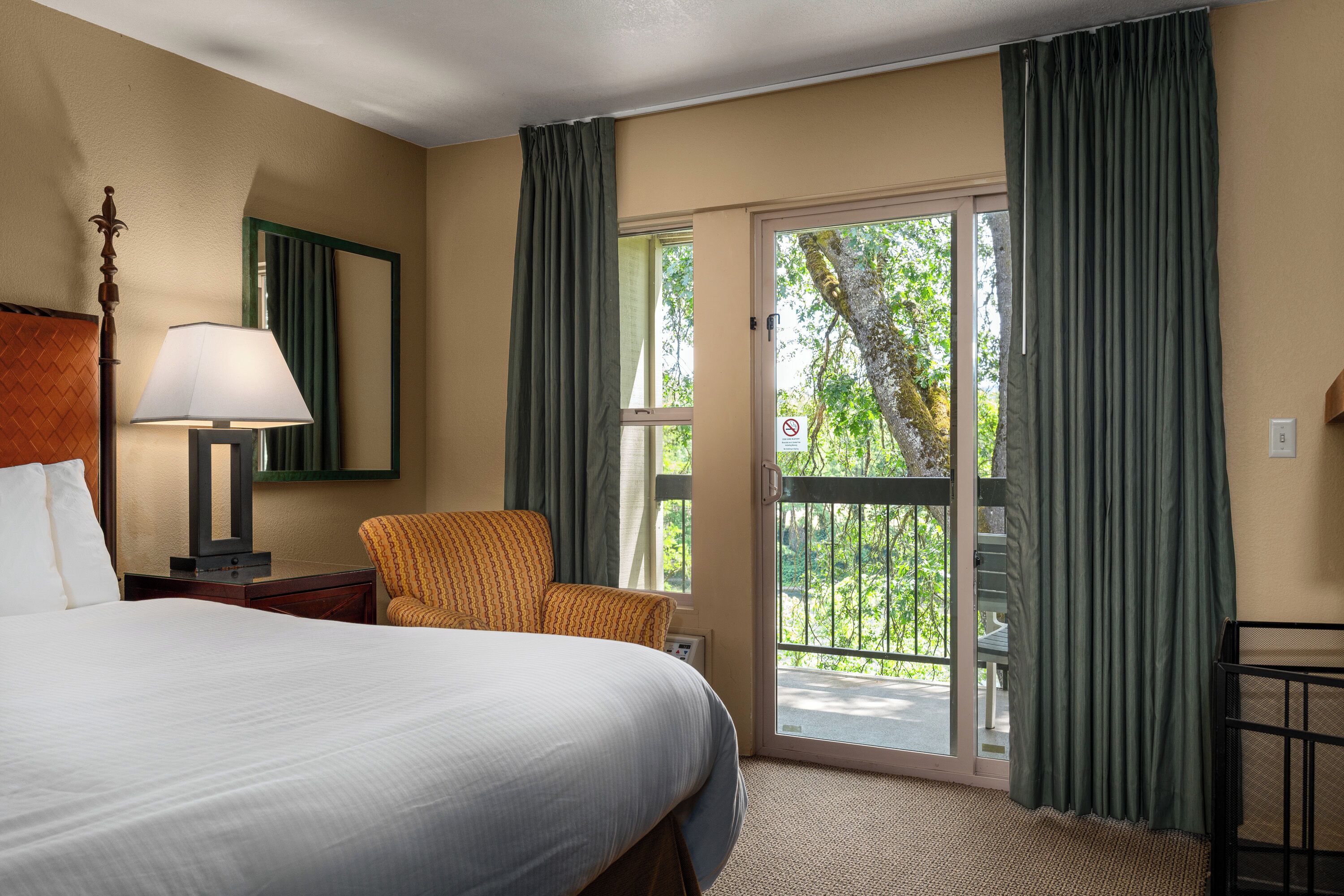 A hotel room with a bed, a chair, a lamp, a window, and a balcony.