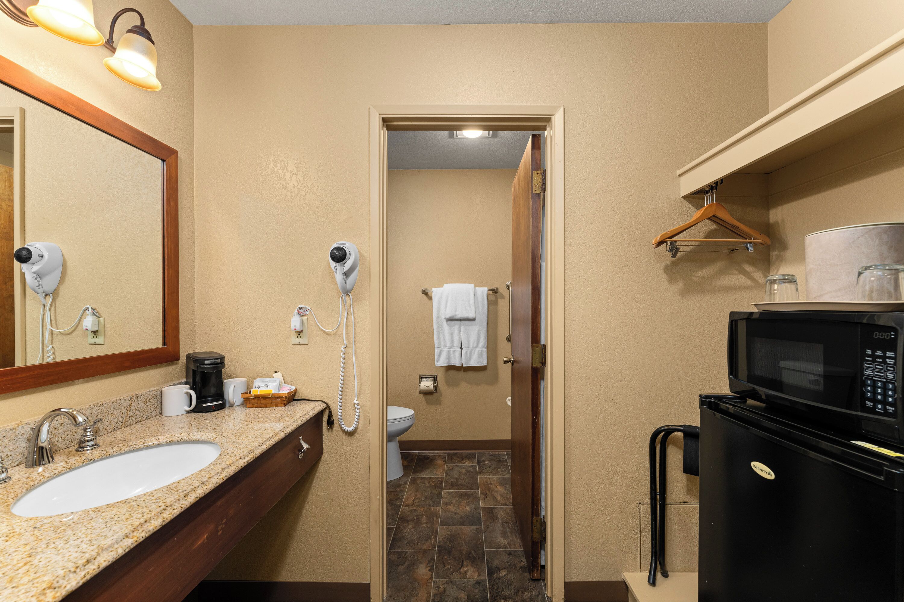 A bathroom with a sink, mirror, hair dryer, towel rack, toilet, and a refrigerator.