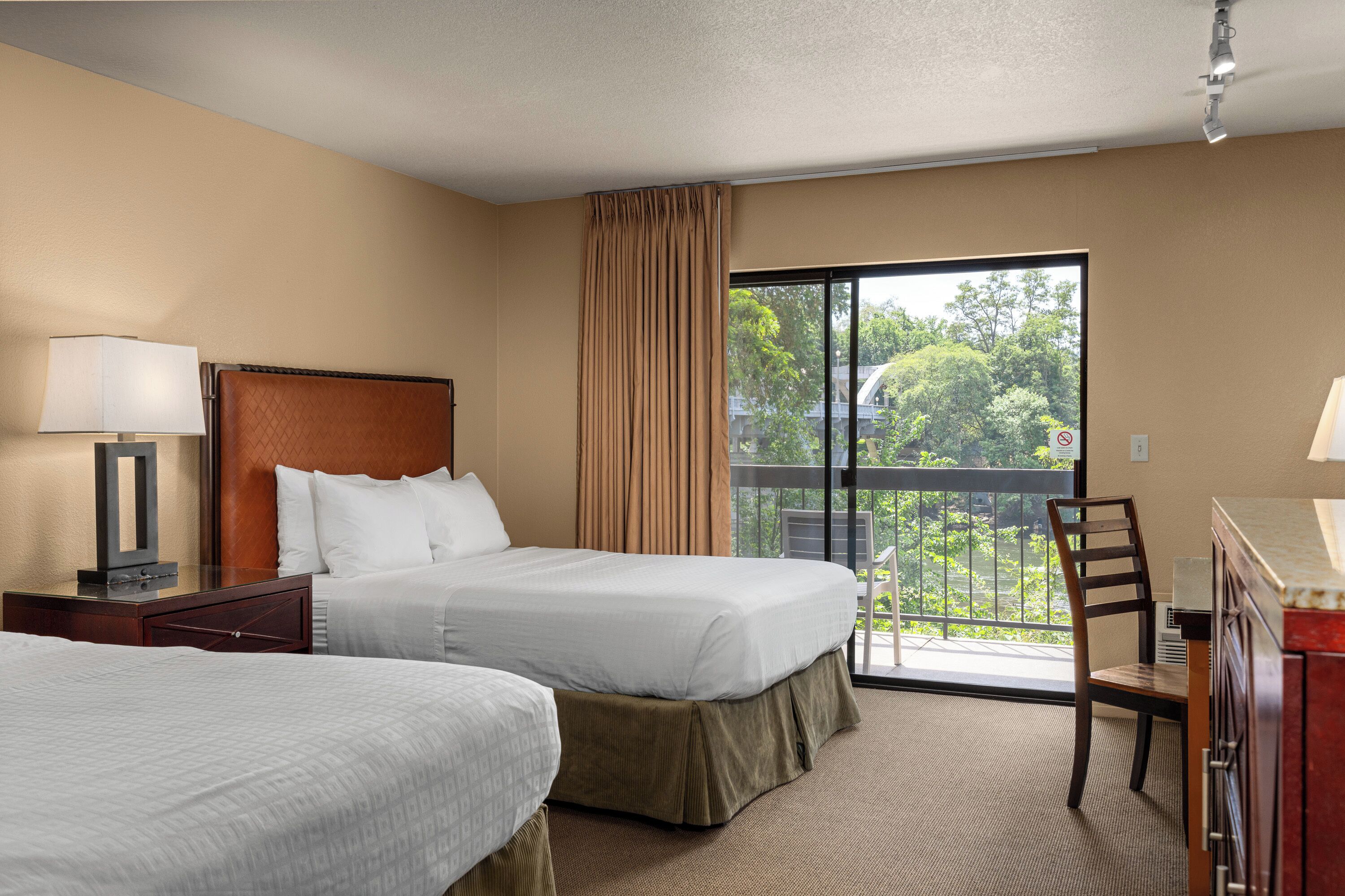 A hotel room with two beds, a desk, a chair, and a balcony with a view.