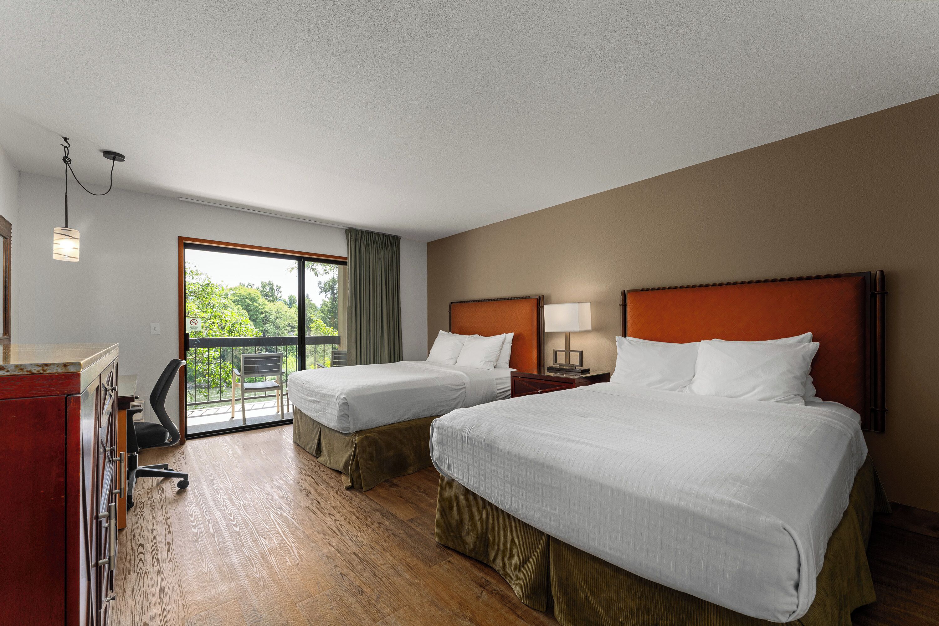 A hotel room with two beds, a desk, a chair, a window with a view, and a balcony.