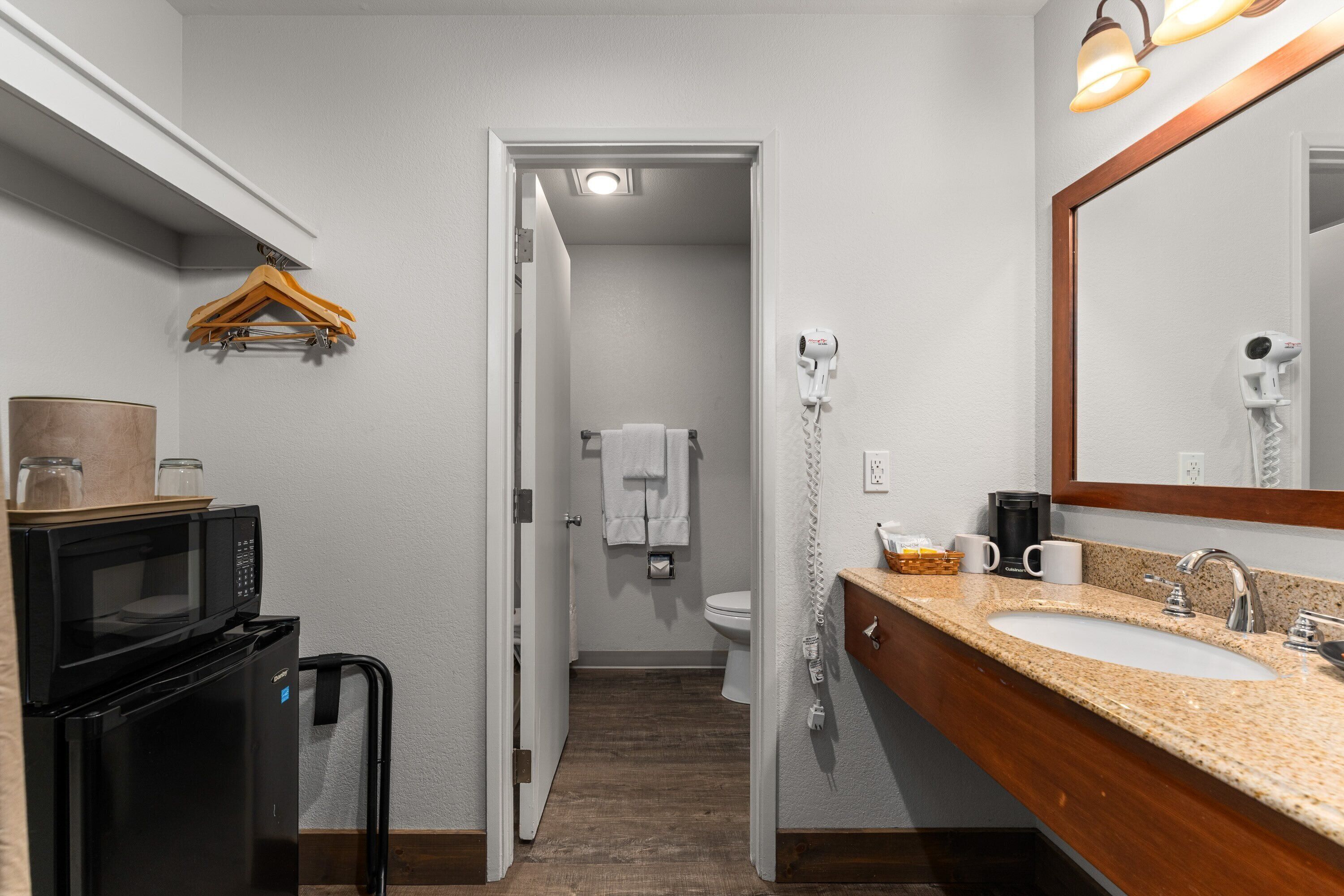 Un baño de hotel con lavamanos, espejo, toallero y secador de pelo.