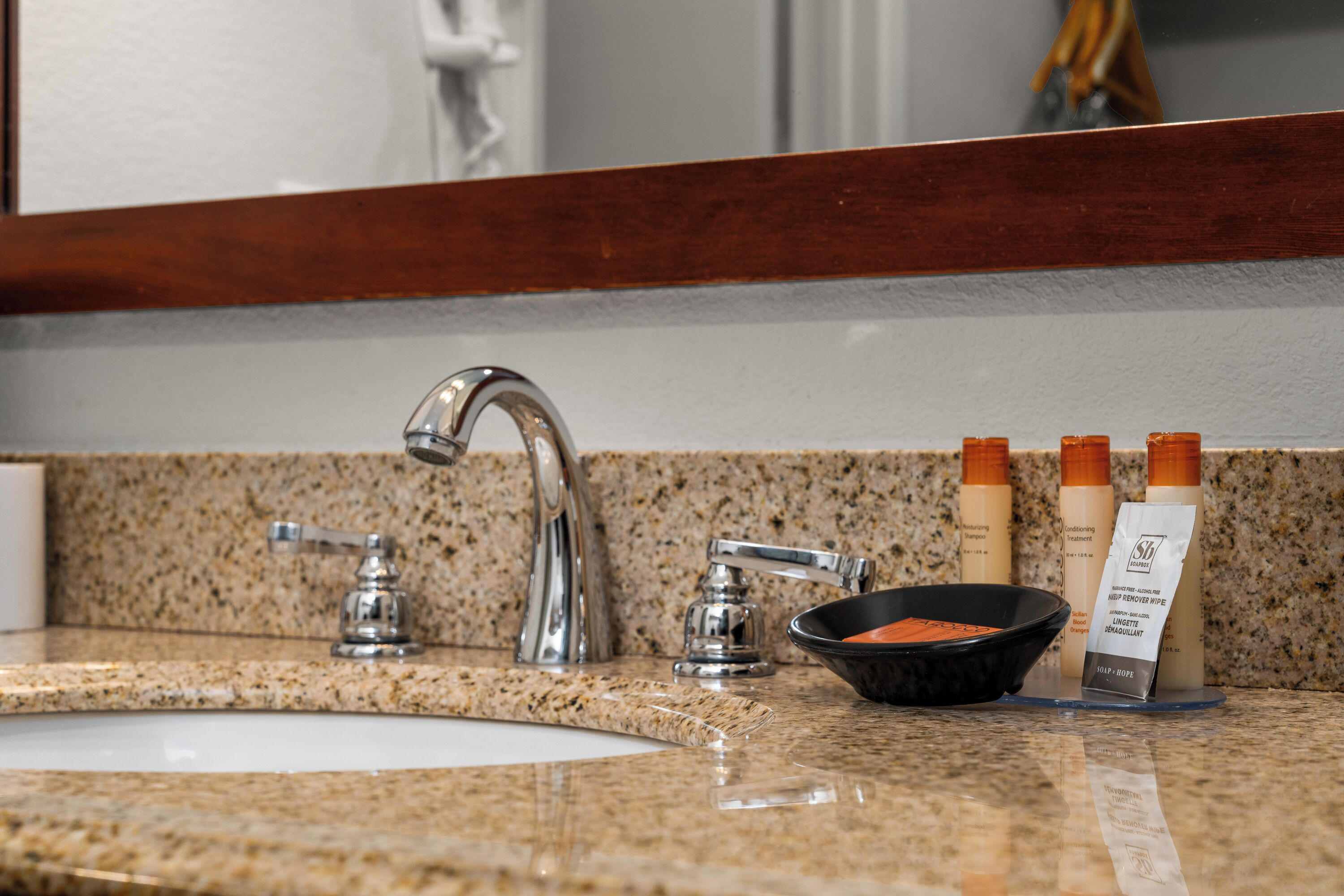A bathroom sink with a granite countertop, two faucets, and three toiletries.
