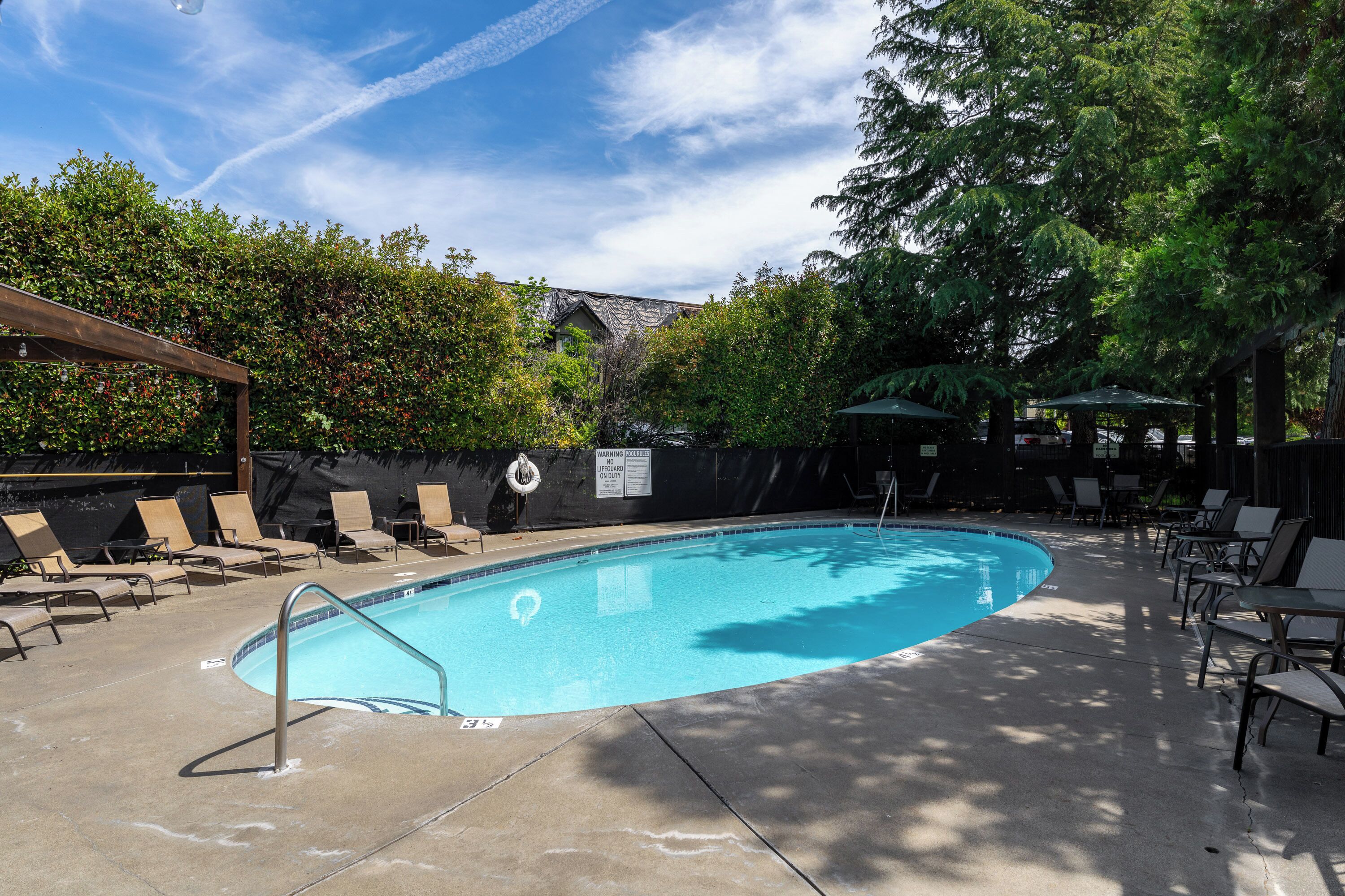 A swimming pool with lounge chairs and umbrellas, surrounded by trees and a covered area.