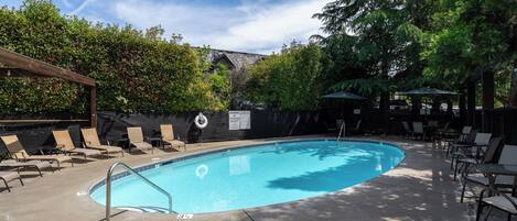 A swimming pool with lounge chairs and umbrellas, surrounded by trees and a covered area.