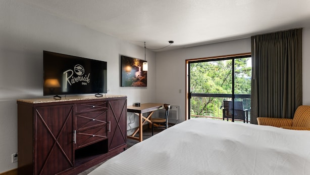 Habitación de hotel con cama, escritorio, televisor y ventana grande.