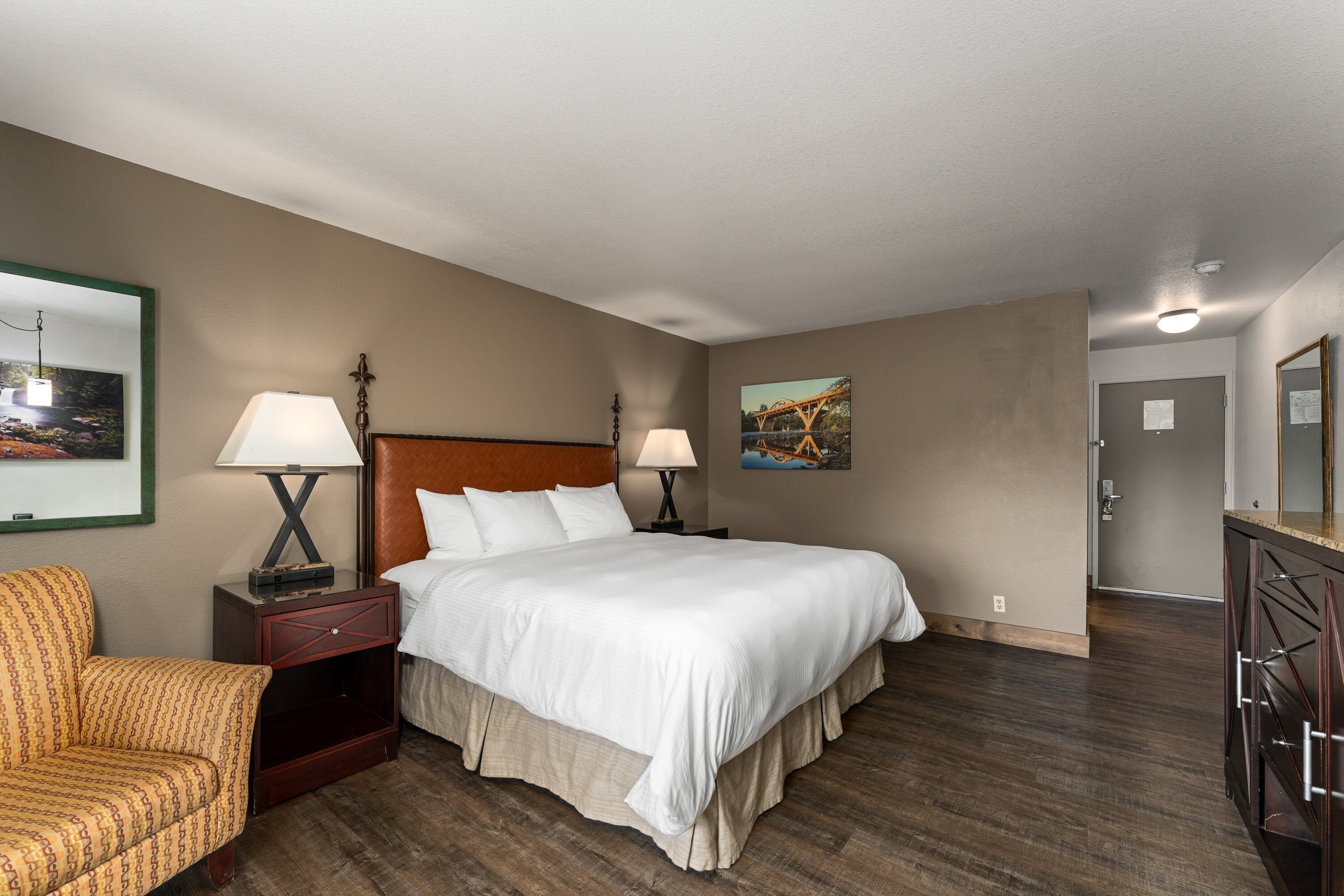 A hotel room with a bed, nightstands, a chair, and a dresser.