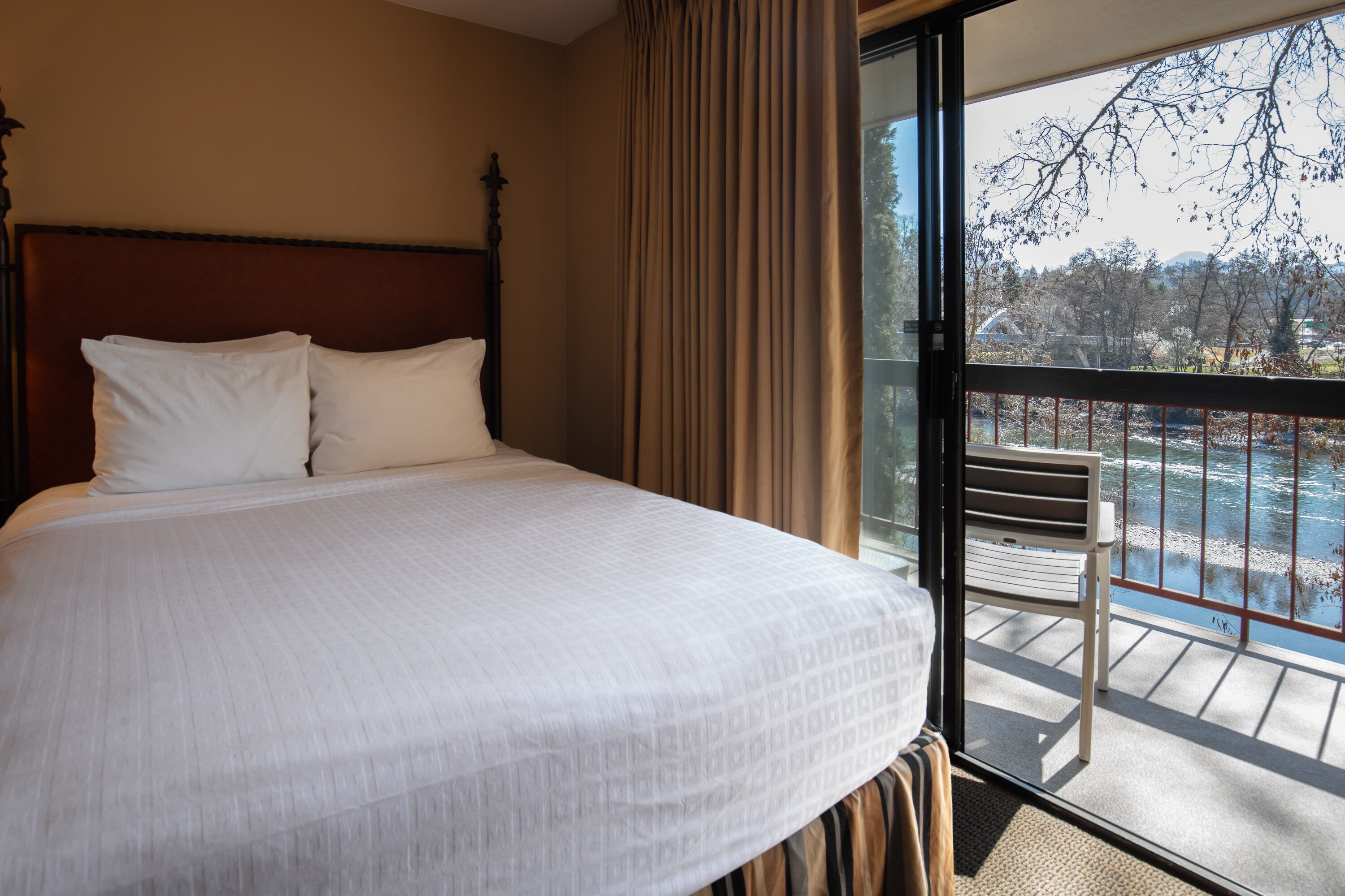 A hotel room with a large bed, a wooden headboard, and a balcony with a view of the outdoors.