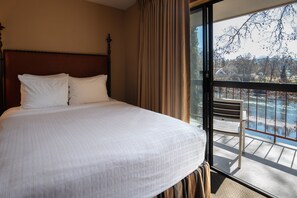 A hotel room with a large bed, a wooden headboard, and a balcony with a view of the outdoors.
