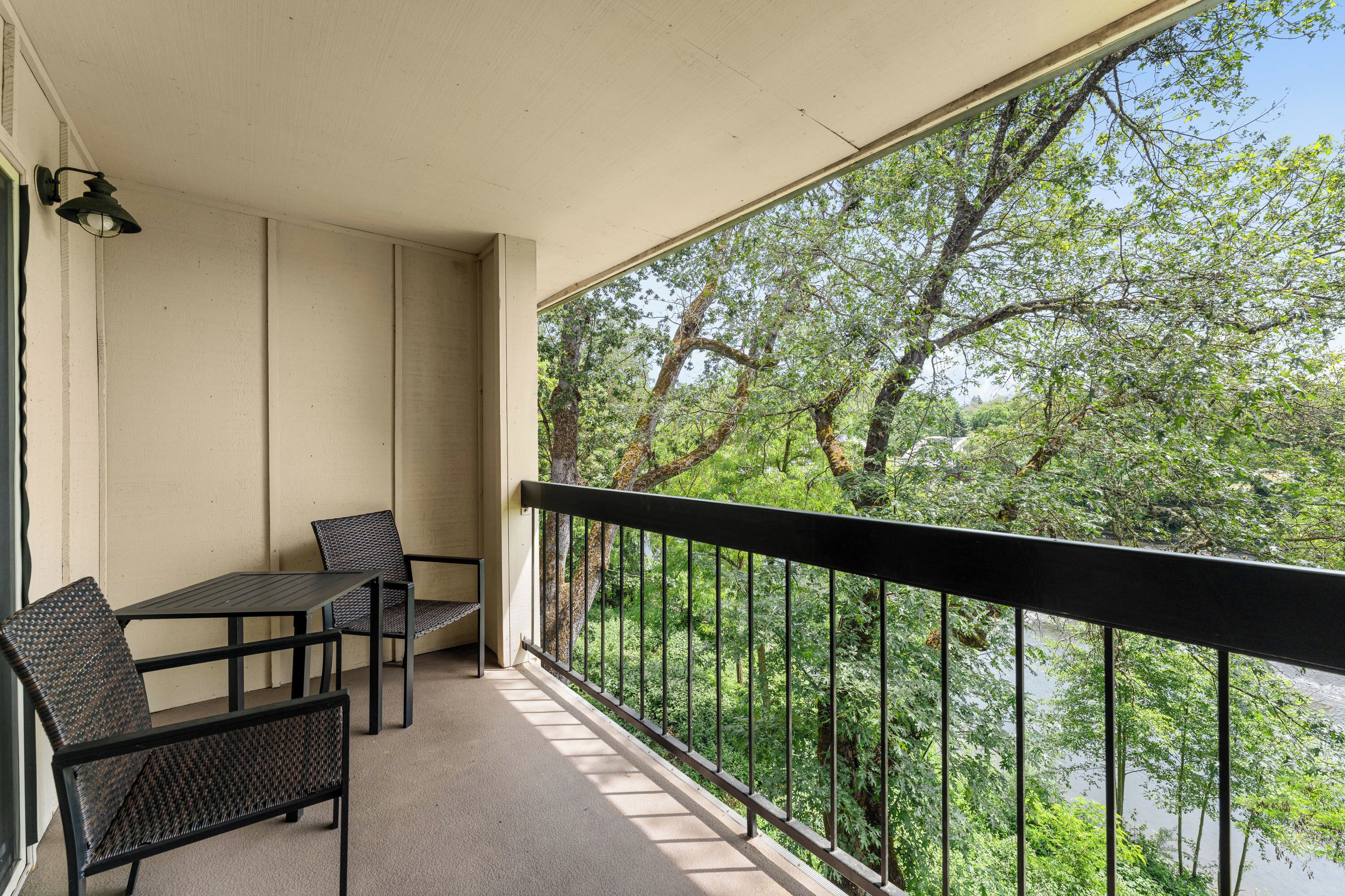 Un balcon avec une table et des chaises, une balustrade et une vue sur des arbres et une rivière.