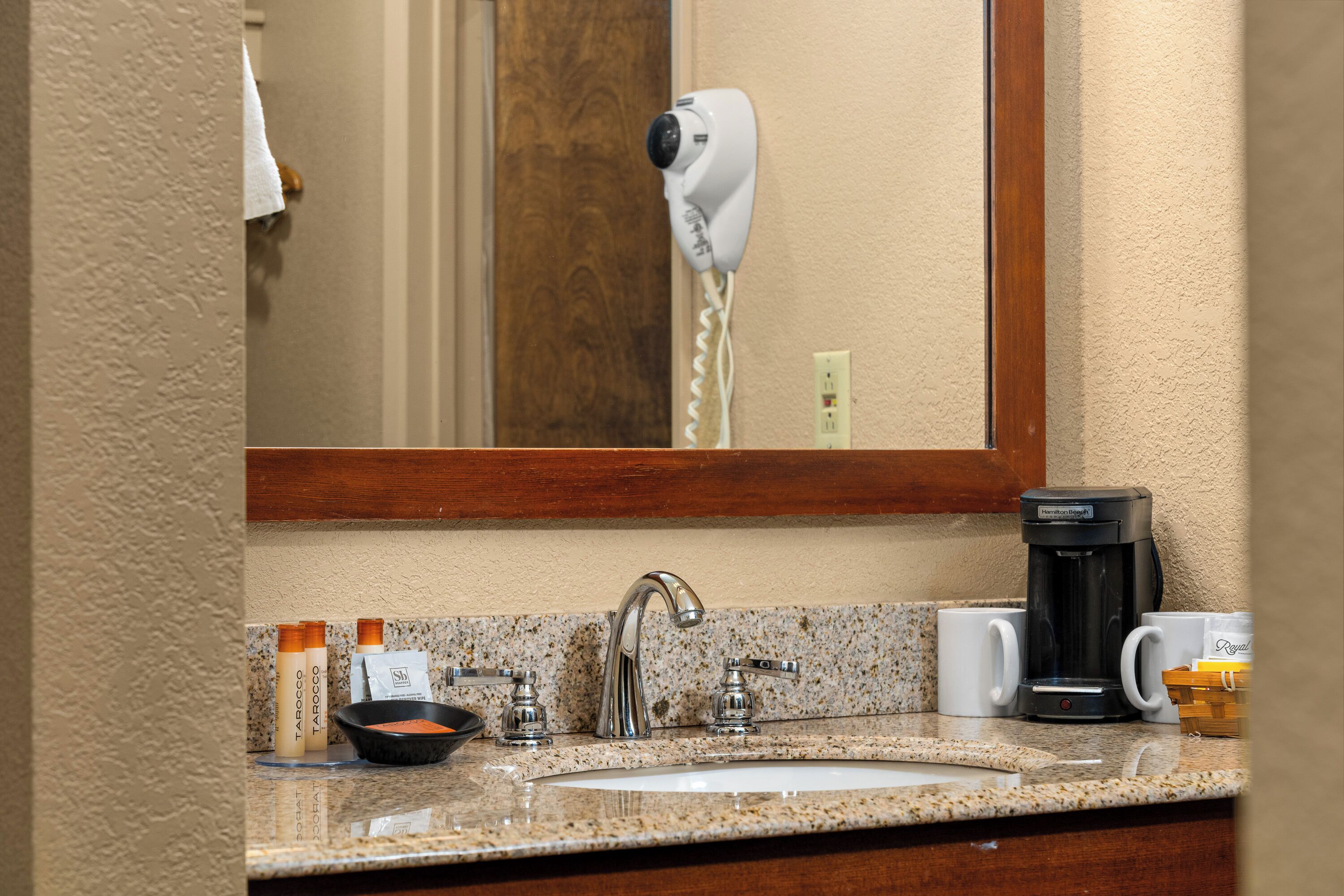 A bathroom with a sink, a hair dryer, a coffee maker, and toiletries.