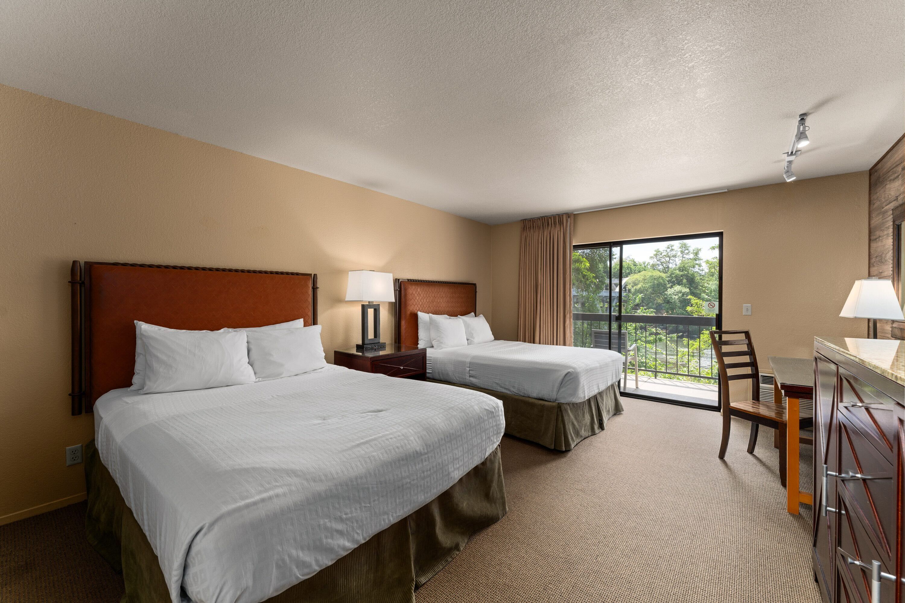Ein Hotelzimmer mit zwei Betten, einem Schreibtisch, einem Stuhl und einem Balkon mit Blick.