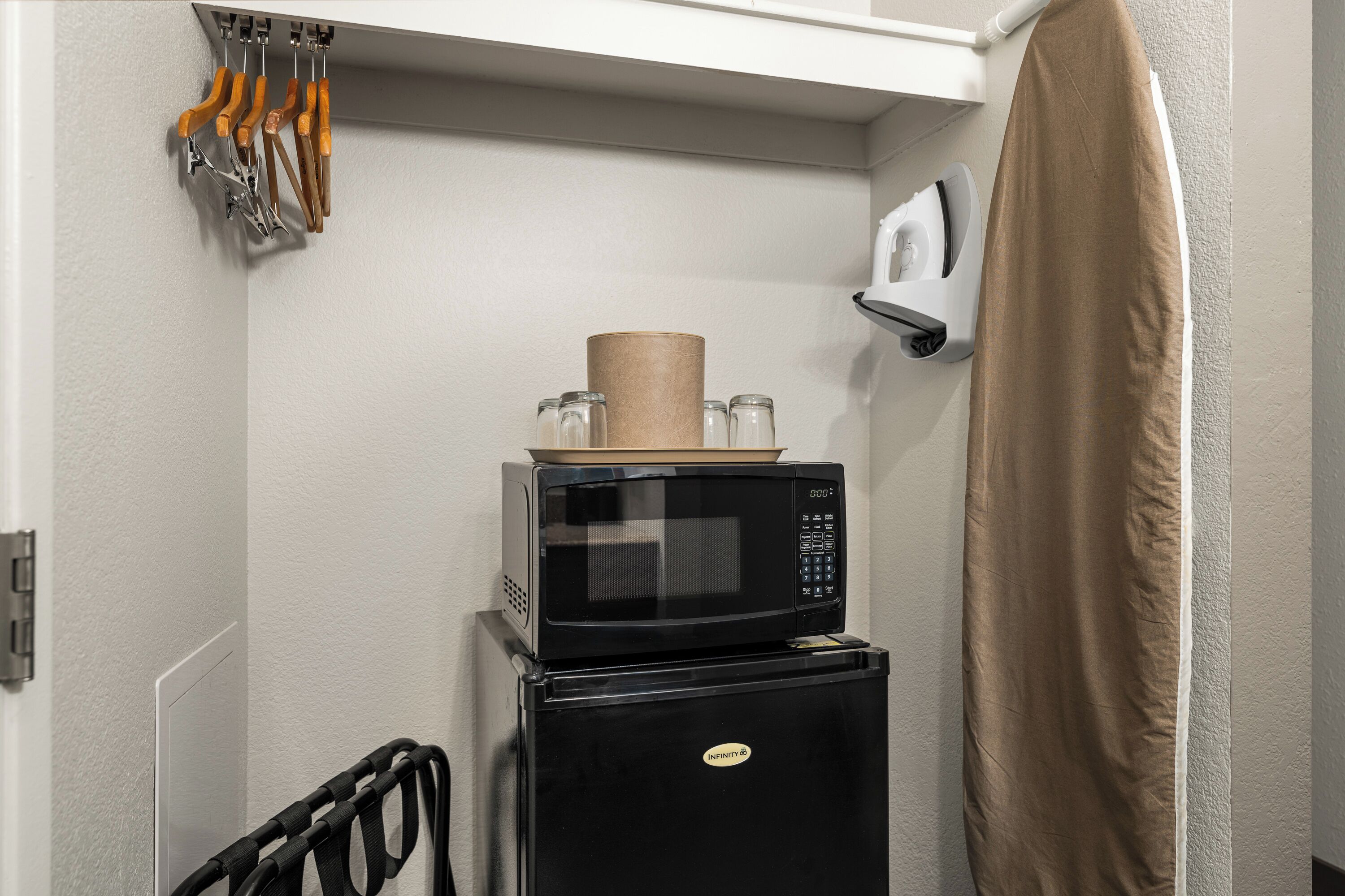A compact kitchen with a microwave and refrigerator, a towel rack with utensils, and a shower curtain.