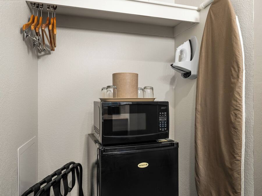 A compact kitchen with a microwave and refrigerator, a towel rack with utensils, and a shower curtain.
