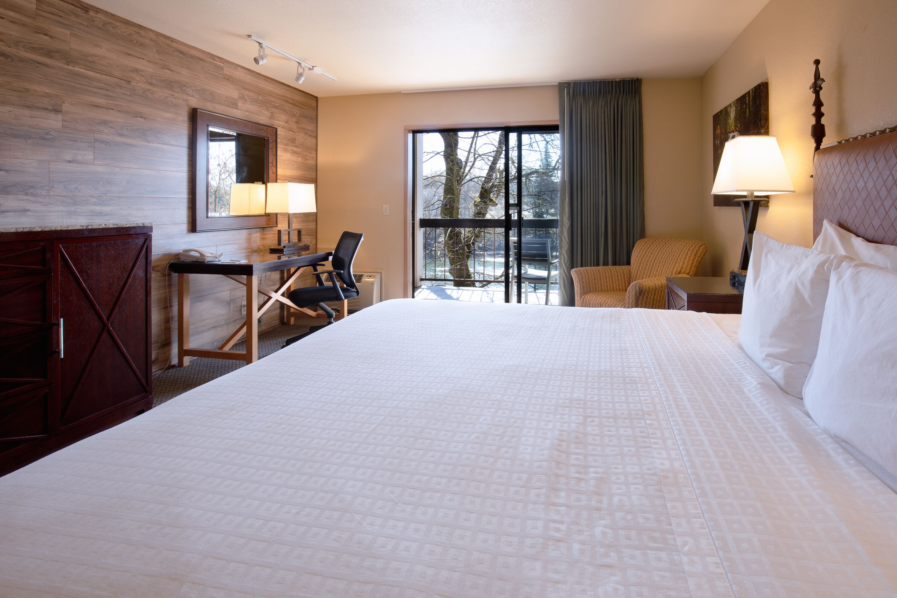 Une chambre d’hôtel avec un grand lit, un bureau avec une chaise, une petite table et une fenêtre donnant sur des arbres.