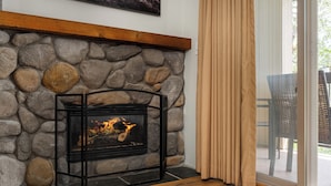 Una chimenea de piedra con estructura metálica negra, repisa de madera y fuego encendido.